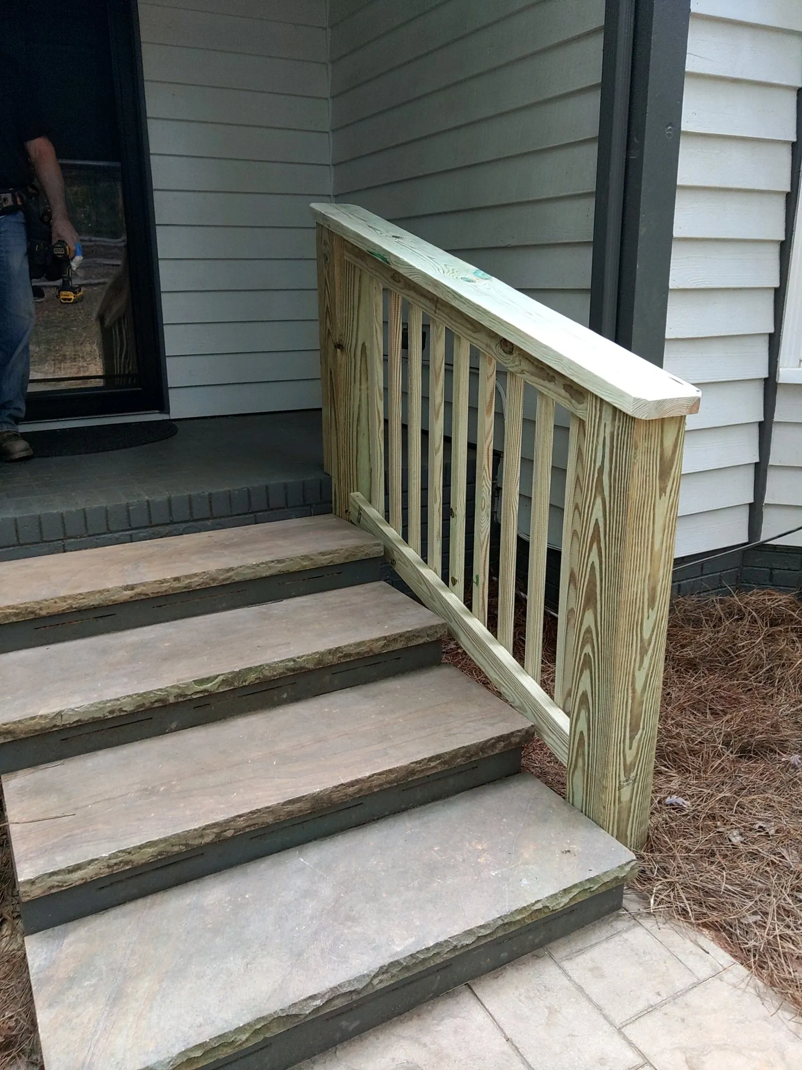 A newly built pressure-treated wood railing and rebuilt stone steps on a Carolina Pro Restoration porch project